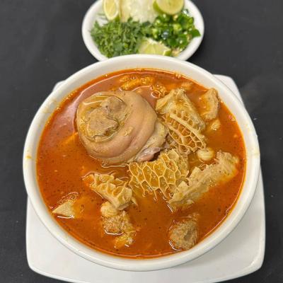 Bowl of Menudo soup wiht chopped onions, cilantro and lime wedges on the side.