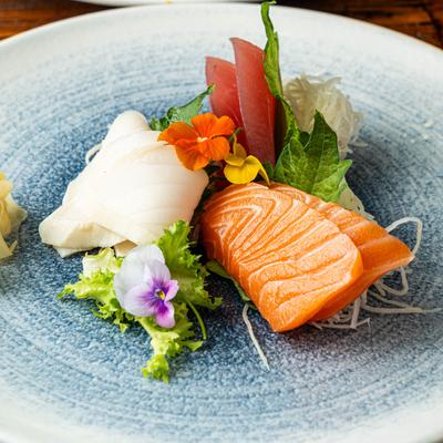 Assorted sashimi, including salmon, white fish, and tuna, garnished with flowers and herbs.