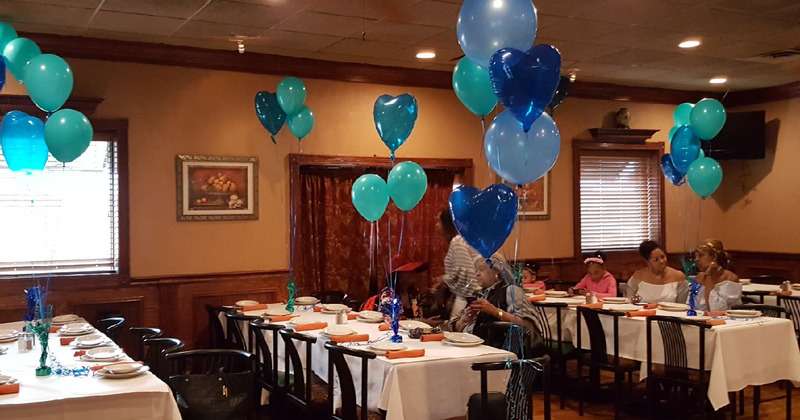 A birthday celebration, guests sitting at set tables decorated with balloons