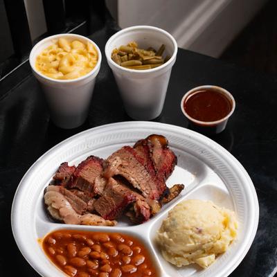 Brisket  with ranch beans and potato salad on a plate, accompanied with sides.