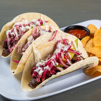 Beef tacos with pickled onions and sauce, served with tortilla chips and salsa.
