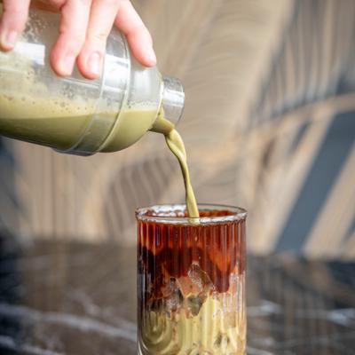 Layered iced coffee with cream being poured in a glass.