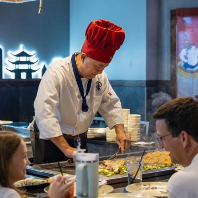 Interior, a chef cooking food for a group of guests sitting around a table.