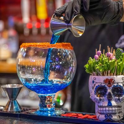 Bartender pouring blue liquid into a glass from a jigger.
