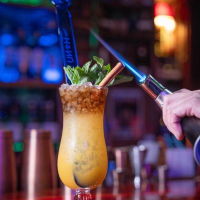 Tropical cocktail being torched, garnished with mint and cinnamon.