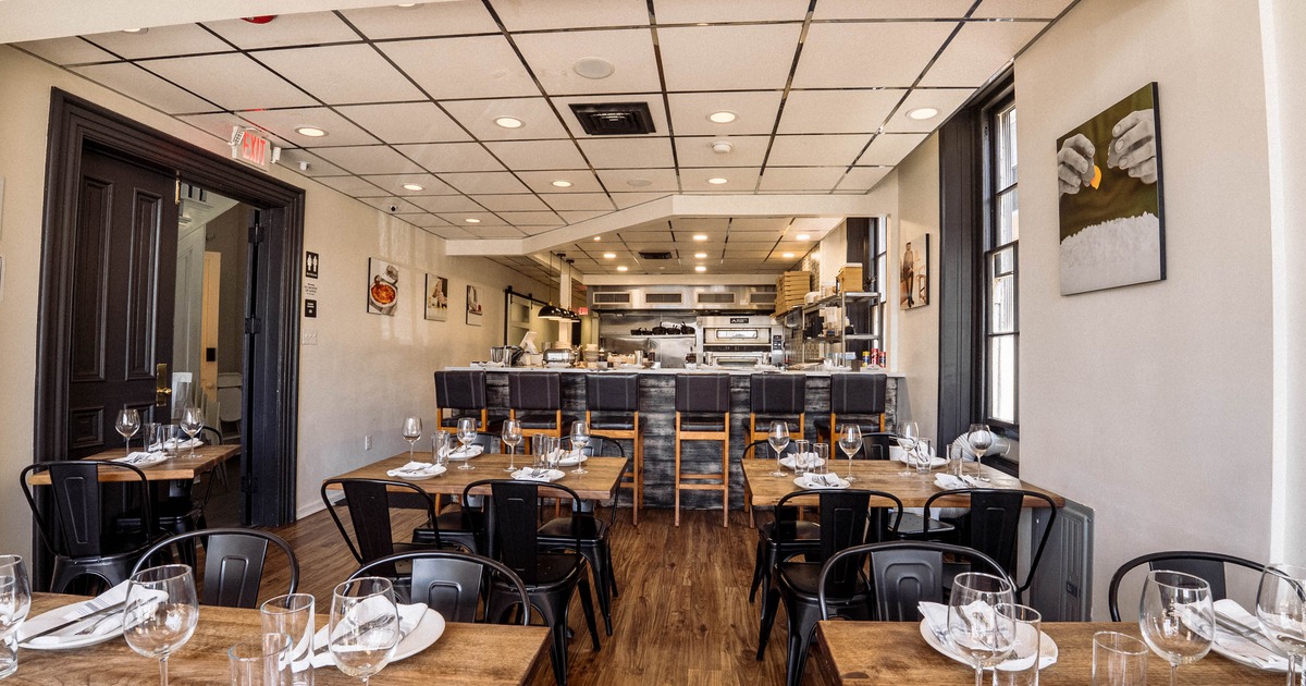 Interior - wooden tables, black metal chairs, an open kitchen and food-themed artwork on the walls