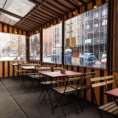 Outdoor dining shed with tables and rain-streaked windows overlooking the street.