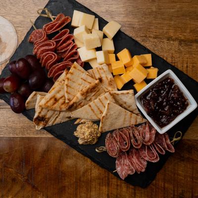 Charcuterie board with cold cuts, cheese, grapes, and pita chips.