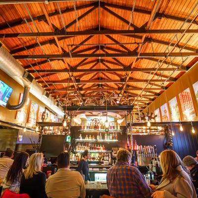 Busy bar interior with wooden ceiling and seated guests.