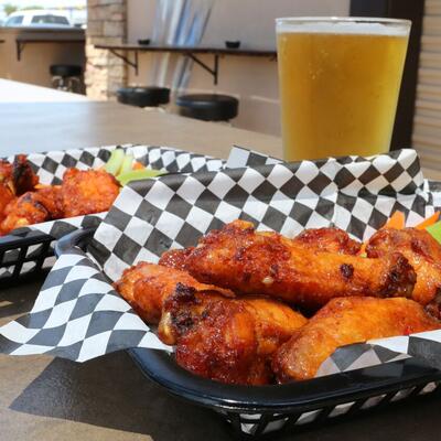 Two plates of grilled chicken with salad, dips on the side, glass of beer in the back