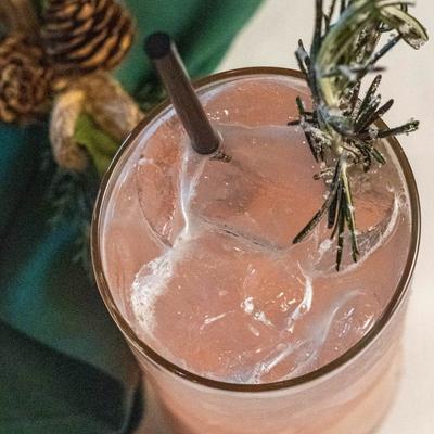 A pink cocktail with ice and a sprig of rosemary.