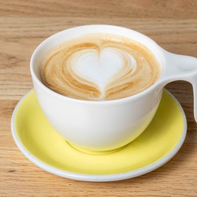 Coffee with heart-shaped latte art, served in a white cup on a yellow saucer.