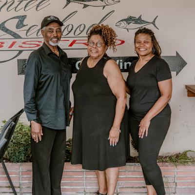 Owners posing in front of a restaurant wall sign.