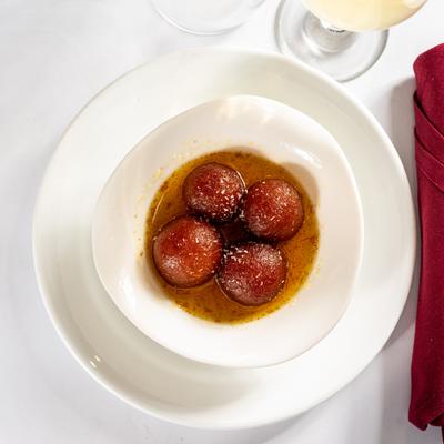 Gulab jamun on a white plate next to a glass of white wine.