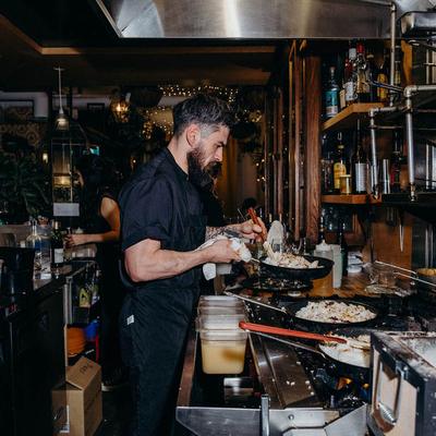 Kitchen staff frying food in frying pans.
