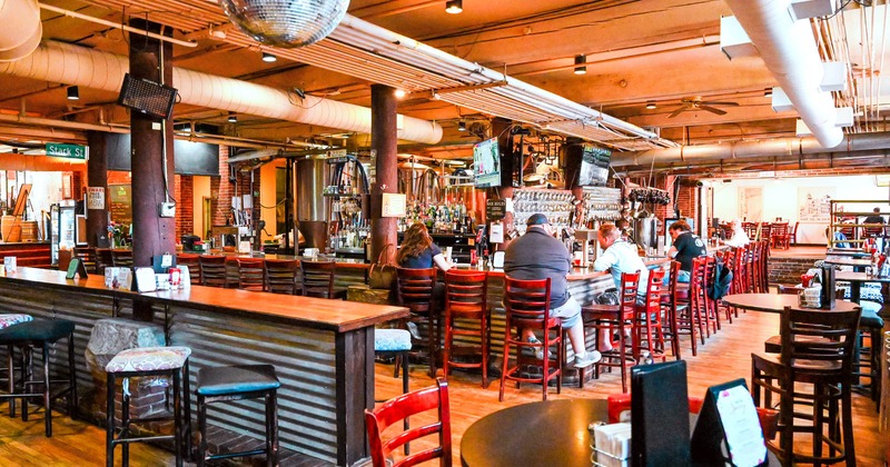 Bar interior with guests sitting, high-top seating, and a disco ball