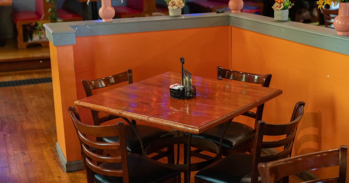 A wooden table with four chairs in a restaurant, set against orange walls with decorative flowers on the partition