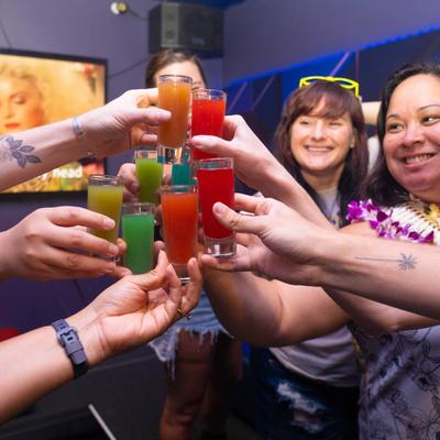 A group of people toasting with colorful shots in a party setting.