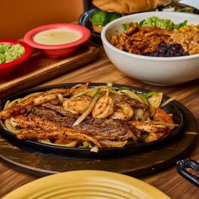 Steak, chicken, and shrimp fajitas served with side dishes.