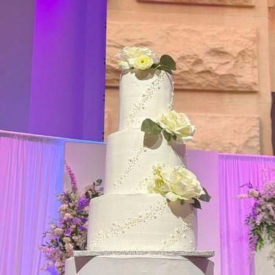 White tiered wedding cake accented with sugar pearls and white roses.