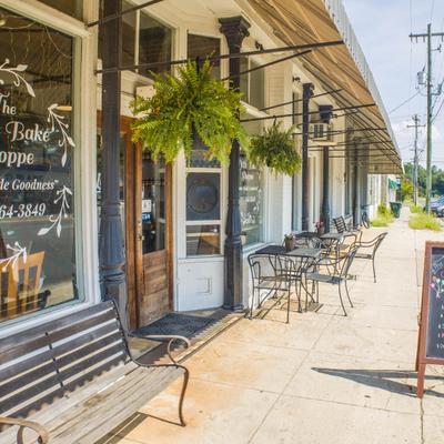 Storefront with a wooden bench, hanging fern baskets, and sidewalk patio tables.