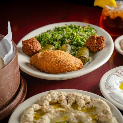 A plate with with veggie grape leaves, kibbe, tabouli, and falafel, dip plates and a tea.