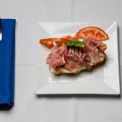 Prosciutto and cheese on a slice of crostini bread, garnished with tomato slices