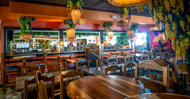 Warmly lit restaurant dining room with wooden tables, woven pendant lamps, mirrors