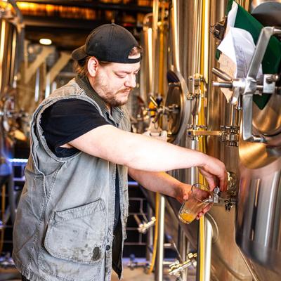 A person pouring beer from a stainless steel brewing tank into a glass.