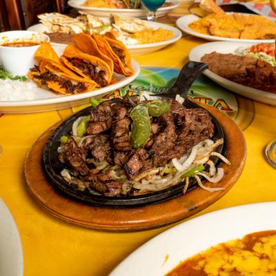 Steak fajitas, birria tacos, quesadillas, and various other dishes spread on a table.