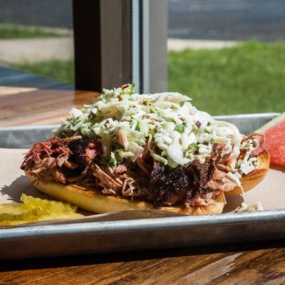 A tray with Pulled pork sandwich topped with creamy coleslaw on a toasted bun.