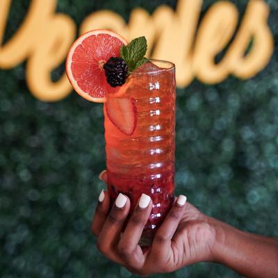 A hand holding a colorful cocktail with strawberries, grapefruit, blackberries, and mint.