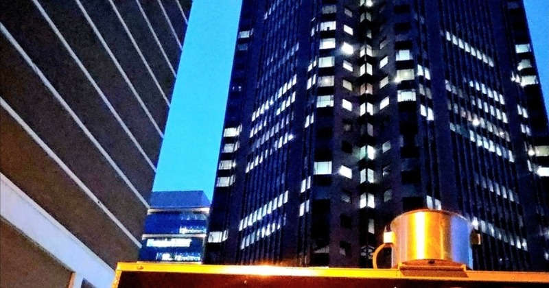 Tall city building with illuminated & Cheese To-Go food trailer at night