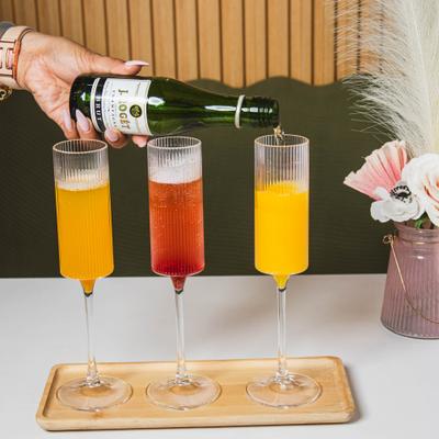 Three Mimosas sitting on a wooden serving tray while being topped with a sparkling wine.