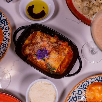 Baked lasagna topped with a purple flower, surrounded by side dishes and drinks.