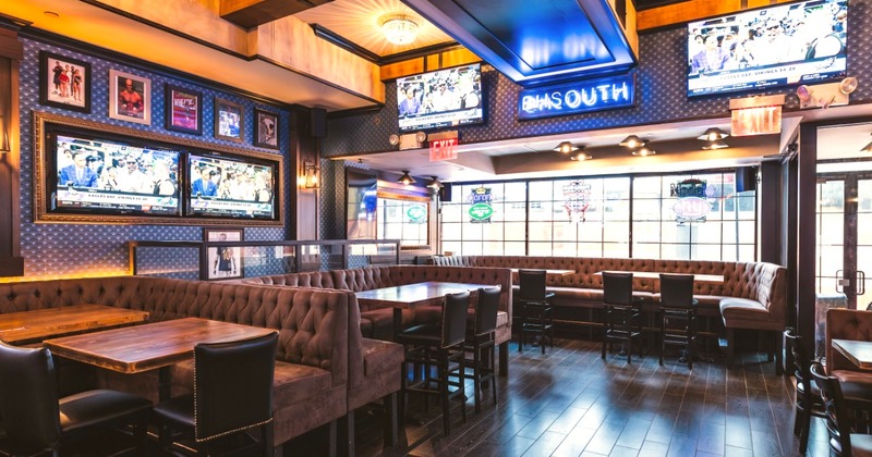 Interior with booths, large windows, TVs showing sports, and a neon sign