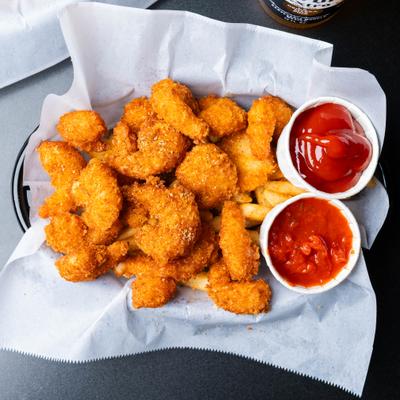 Coconut shrimp served over fries in a basket with ketchup and cocktail sauce.