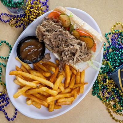 Roast Beef Poboy with tomato and pickles, fries and sauce on the side.