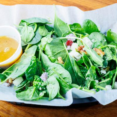 Spinach salad with a vinaigrette dressing served in a side cup.
