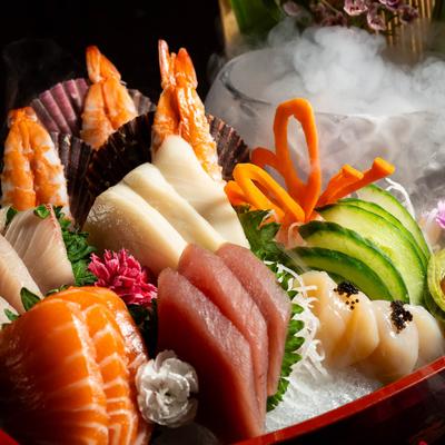 Assorted sashimi with shrimp, tuna, salmon, and garnishes served over ice with dry ice fog.