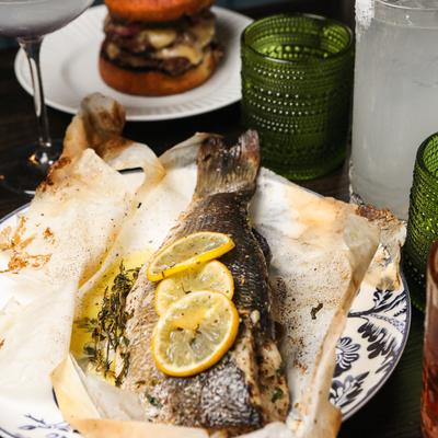 Whole baked fish, topped with lemon slices, served in parchment paper.