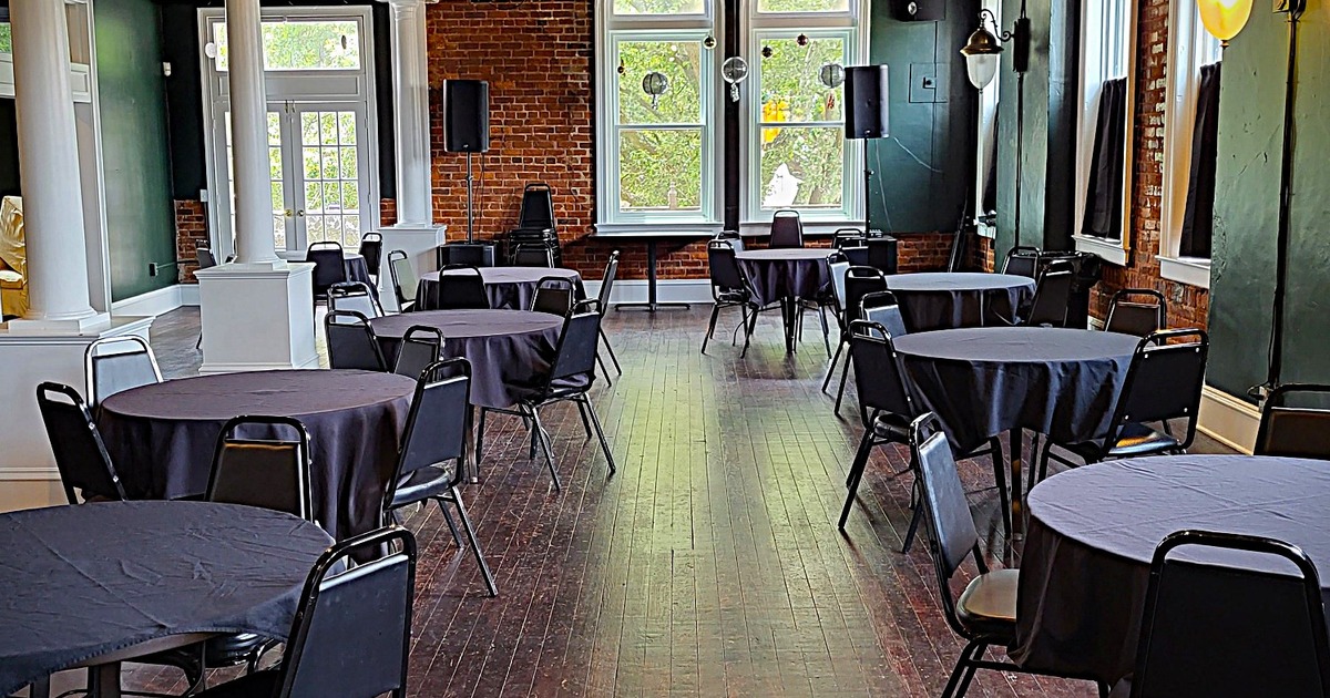 Spacious room with round tables covered in black tablecloths and empty chairs