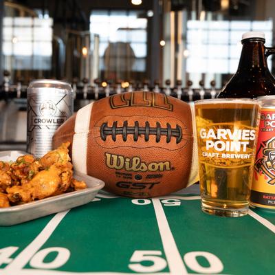 Chicken wings, beer, and football on table in a  brewery setting.