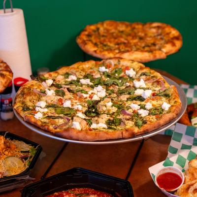 Pesto Supremo Pizza served on a stand alongside other food items.