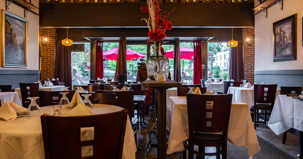Elegant interior - white-clothed tables, dark wood furniture, red curtains, hanging lights.