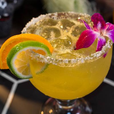 Margarita with a salted rim, garnished with citrus slices and a purple orchid.