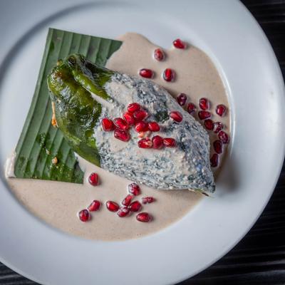 Stuffed poblano pepper topped with walnut salsa and pomegranate seeds.