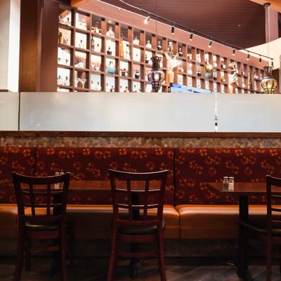 Interior view of a restaurant dining area with a bottle display shelf, booth seating, and chairs.