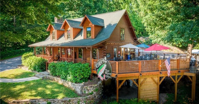 Rustic log cabin restaurant with a wraparound deck, red umbrellas, and American flag
