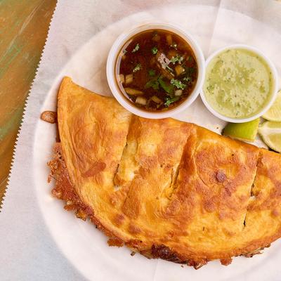 Quesabirria tacos, served with lime, broth, and salsa.